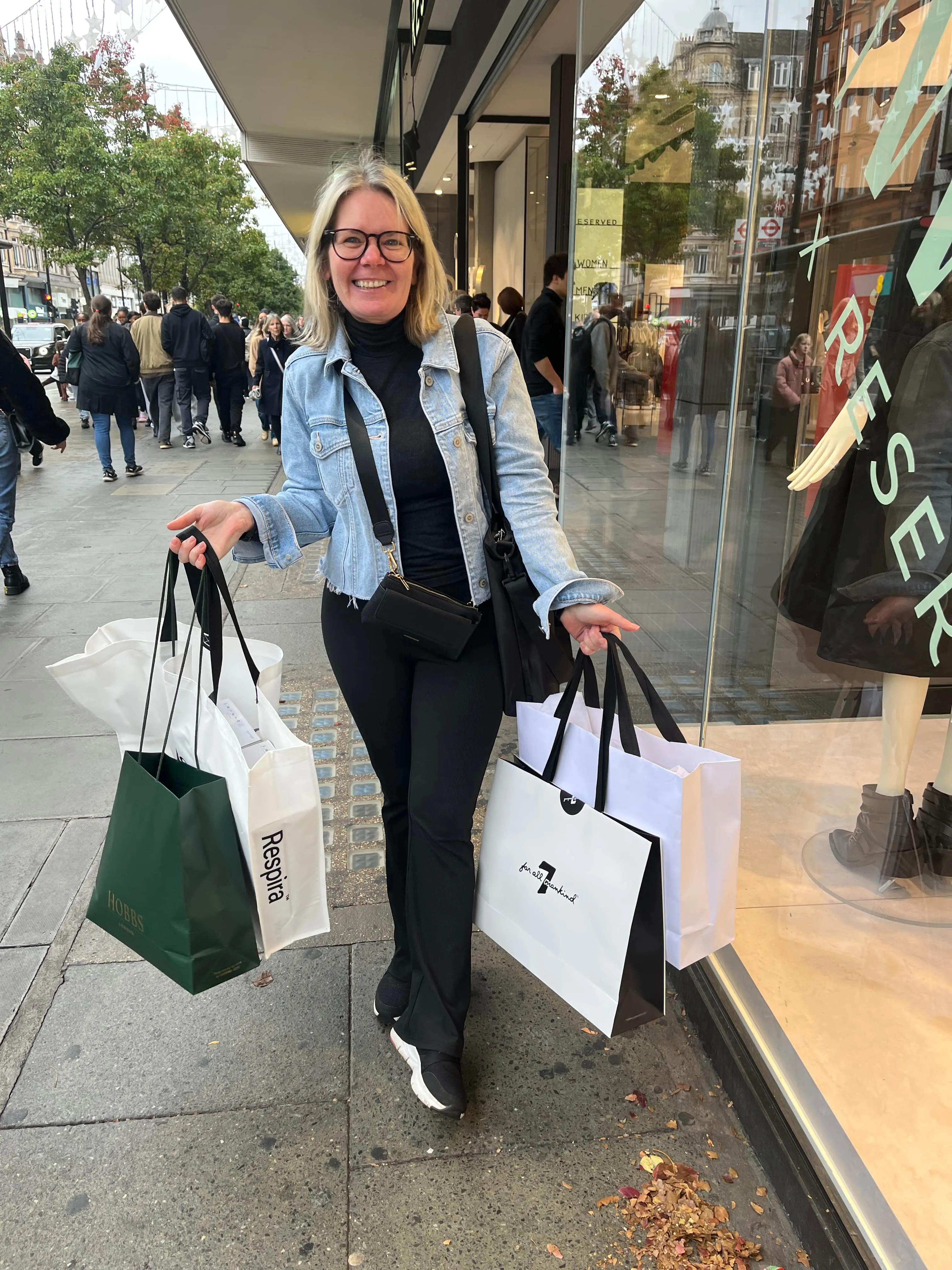 A smiling client on a London street carrying four shopping bags after personal shopping