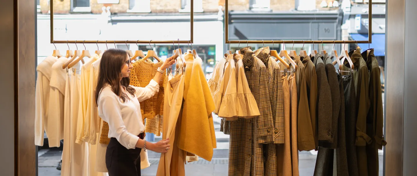 Maria choosing a piece from a rail of clothes in a boutique window