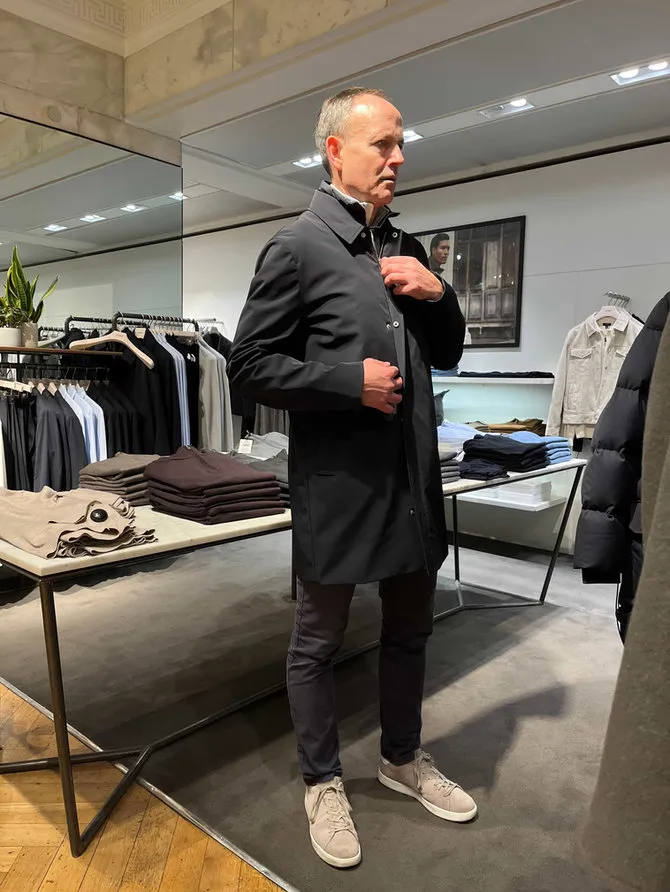 A client trying on a dark mac in a menswear store during men's personal shopping