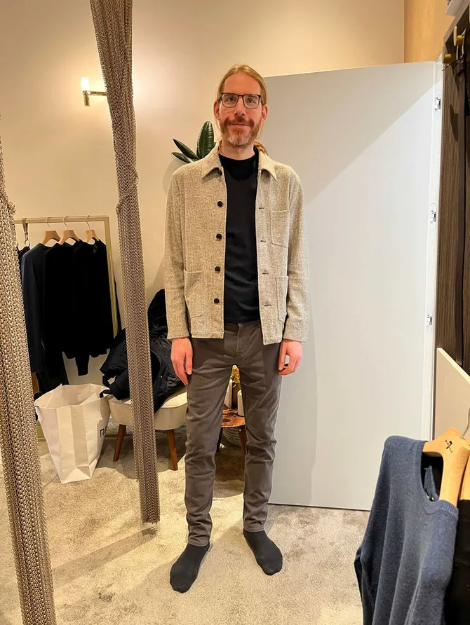 A client in a fitting room wearing a textured overshirt and grey trousers