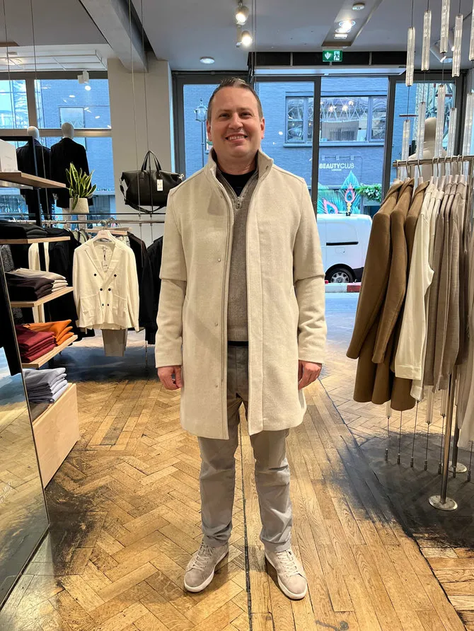 A smiling client trying on a cream overcoat in a menswear store