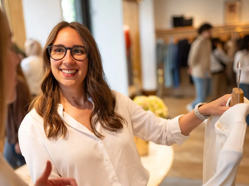Maria Pastor smiling as she shows a client a white top in a boutique