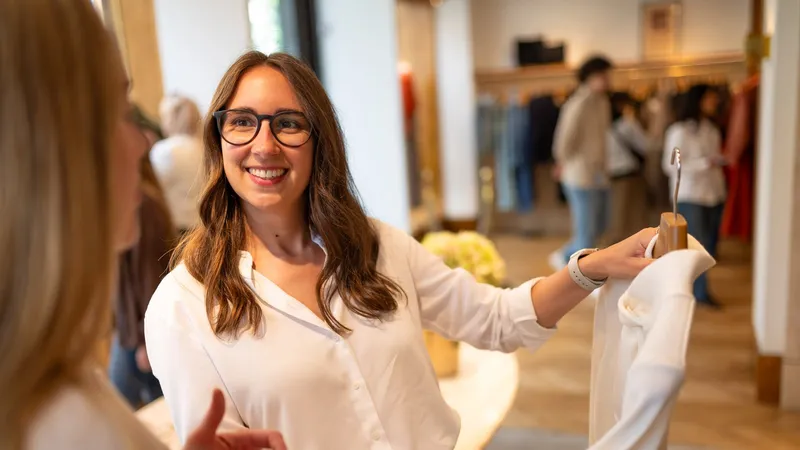 Maria Pastor smiling as she shows a client a white top in a boutique