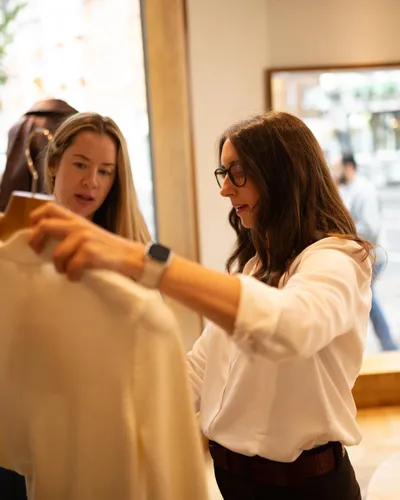 Maria Pastor holding up a cream shirt for a client to consider in a shop