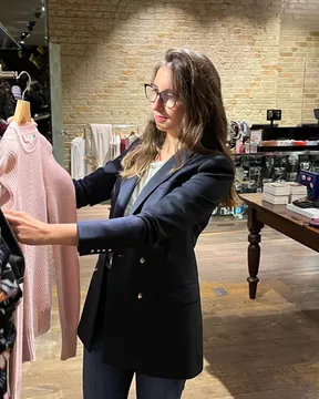 Stylist in a navy blazer holding up a blush knit in a brick-walled boutique