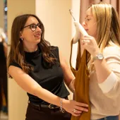 Maria Pastor holding a mustard dress up to a client in a fitting room