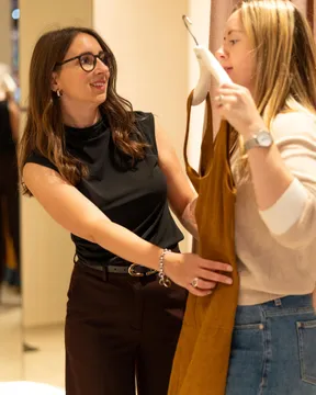 Maria Pastor holding a mustard dress up to a client in a fitting room