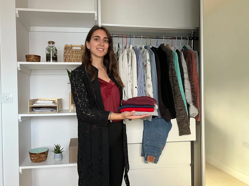 Woman holding a folded stack of clothes in front of an open wardrobe