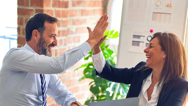 Two colleagues in business dress sharing a high five across a meeting table