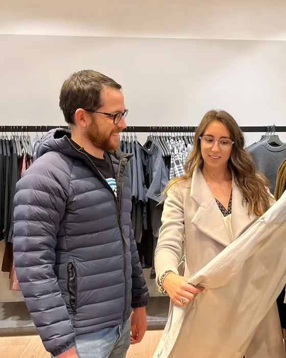 Maria Pastor with a client during a personal shopping session, holding up a cream jacket for him beside a rail of clothes