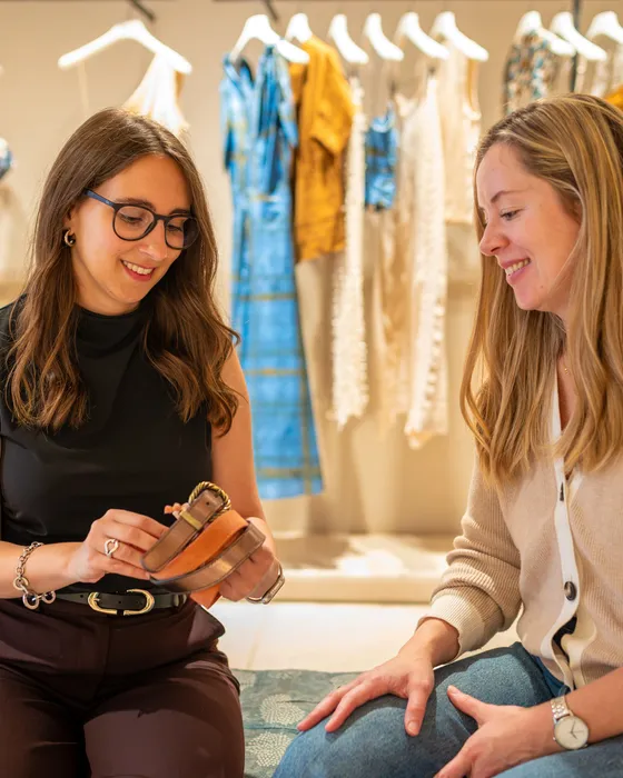 Maria Pastor showing a client a belt in a boutique, the two of them seated and smiling