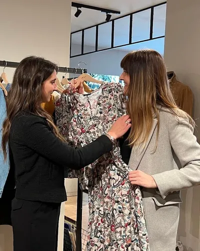 Maria Pastor holding a floral dress up to a client in a boutique