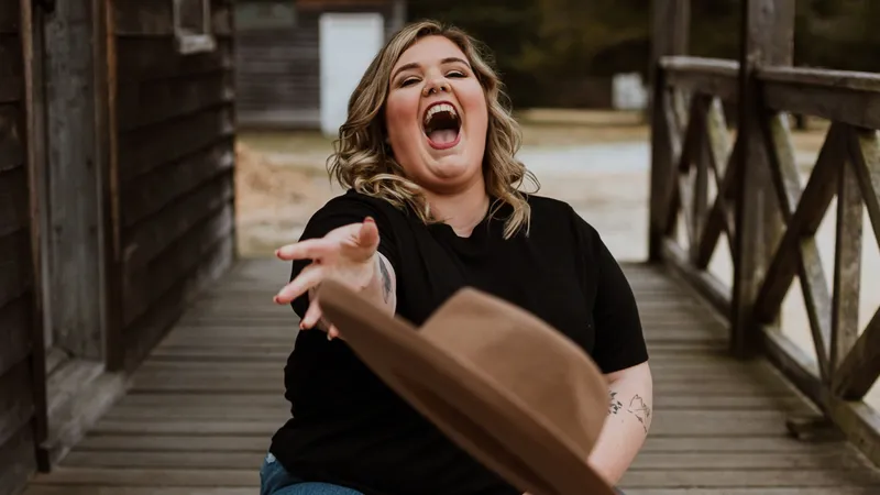 A woman in a black T-shirt laughing as she tosses a brown hat towards the camera